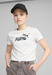 Camiseta blanca corta con el logo y emblema en negro de "PUMA". Combinada con pantalones de tiro alto grises y una gorra negra. Diseño sencillo y casual.