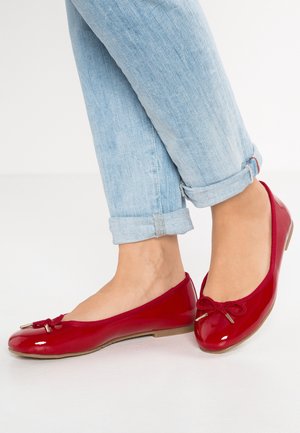 Red patent leather ballet flats with a rounded toe, decorative bow, and small metallic accent, paired with rolled-up light blue jeans.