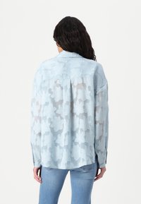 Camisa azul clara com bordado floral, tecido transparente, mangas longas e bainha arredondada, com colarinho clássico e punhos com botão.