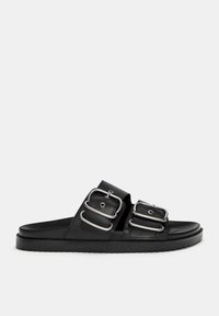 Schwarze Rutsch-Sandalen mit zwei breiten Riemen und silbernen Schnallen, einer glatten matten Textur und einer dicken, flachen Gummisohle.