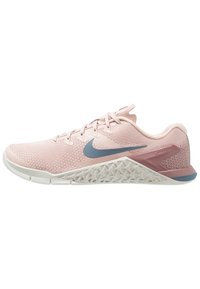 Zapatilla deportiva de color rosa claro con una parte superior de tejido transpirable, detalles en gris y una suela blanca texturizada que presenta un patrón geométrico único.