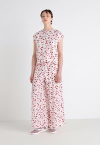 Completo a due pezzi floreale composto da una blusa a maniche corte con vestibilità rilassata e pantaloni a gamba larga, entrambi realizzati in un tessuto rosa chiaro con fantasie di fiori rossi.
