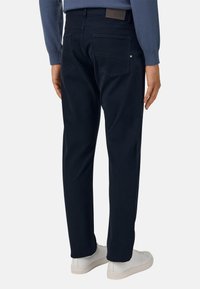 Tumed sinise värvi puuvillasegusest kangast püksid, millel on sirge lõige, tagakotid ja nahast logo täpp vööl. Kantud valgete kingadega.