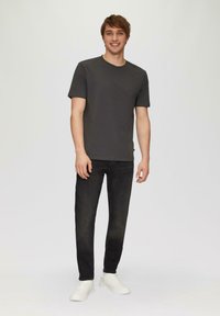 T-shirt à manches courtes gris foncé, associé à un jean noir et des baskets blanches. Tissu lisse, design minimaliste et coupe ajustée.