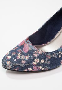 Chaussure plate pour femme en tissu bleu marine à motif floral, bout rond et doublure intérieure bleu foncé sur fond blanc.