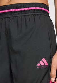 Sorte basketballshorts med en ventileret sort talje, der har en pink stribe, samt et pink Adidas-logo på den nederste venstre side.