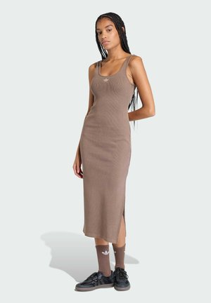 Brązowa prążkowana sukienka na ramiączkach z bocznymi rozcięciami, zestawiona z czarnymi trampkami i brązowymi skarpetkami do kostek z białym logo.