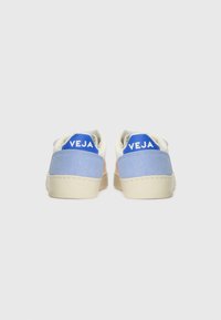 Treninger med en hvit skinnoverdel, blå semsket skinnaksenter og en beige gummisåle. Har en blå hælflik med "VEJA"-logo i hvit tekst.