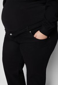 Jeans elásticos pretos com cintura média, apresentando fechamento com botão, bolsos laterais e uma textura suave, projetados para o conforto.