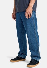 Jeans de mezclilla azul de pierna recta con una textura suave, que presentan un diseño clásico de cinco bolsillos. Combinados con zapatillas negras.