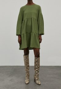 Vihreä, löysä, kerroksittain muotoiltu mekko pitkillä hihoilla; teksturoitu kangas. Yhdistetty polveen saakka ulottuviin käärmeennahkakuosisin saappaisiin, joissa on paksut korot.