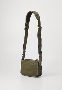 Oliņu zaļš, taisnstūrveida crossbody soma ar teksturētu materiālu, regulējamu jostu un sudraba apdares elementiem. Minimālisma dizains.