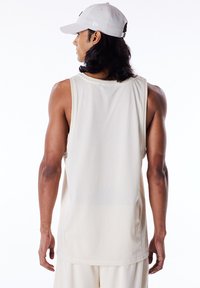 Beige nettoberørt tanktop med løs passform, med rå kanter og rund hals. Viser en pustende tekstur og sidesplitter for bevegelsesfrihet.