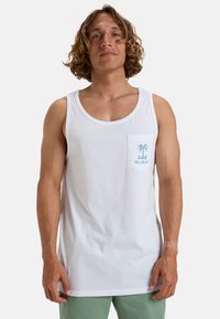 Top de tirantes de algodón blanco con un bolsillo que presenta un gráfico de una palmera azul. El diseño incluye un escote ancho y un corte relajado.