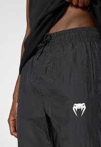 Μαύρα σορτς από αδιάβροχο ύφασμα με ελαστική μέση και κορδόνι, με λευκό λογότυπο φιδιού και διακριτικό υφασμάτινο μοτίβο.