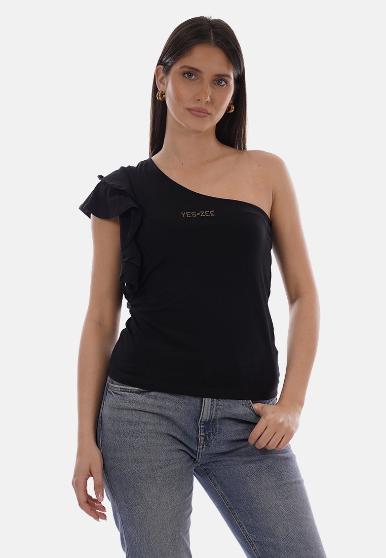 Donna con capelli lunghi e scuri che indossa orecchini a cerchio dorati, un top nero monospalla con dettaglio a rouches e la scritta "YES-ZEE", e jeans blu.