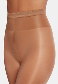 Collant trasparenti color sabbia con una fascia ampia e liscia in vita. Il tessuto ha una finitura lucida e un design senza cuciture che si estende fino a metà coscia.