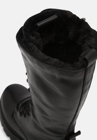 Botín de cuero negro con un suave forro de piel negra. Presenta ojales robustos y cordones, y un diseño de puntera redondeada. Detalle de superficie texturizada.