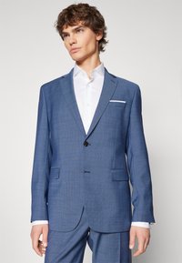 Blauwe geruite blazer met insnijdingen, enkele knoopsluiting en twee frontzakken. Gecombineerd met een witte dress shirt.