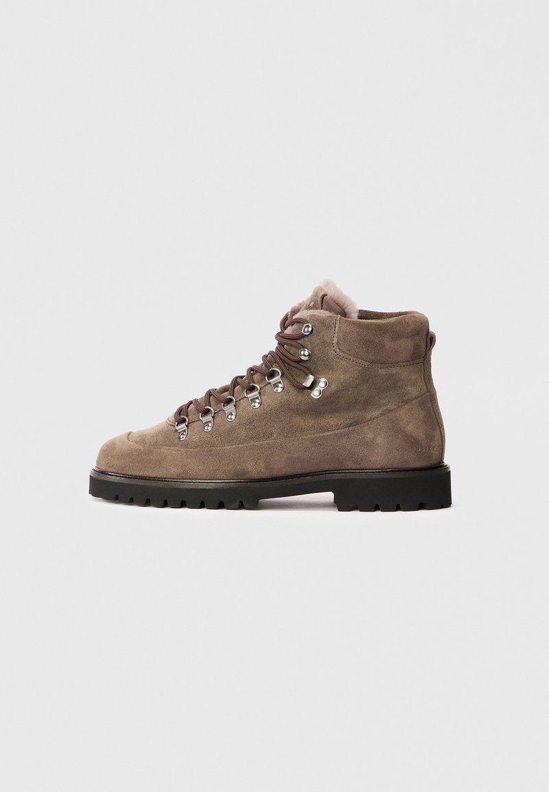 Botte de randonnée en suede marron avec une tige haute, un bout rond, des œillets en métal pour les lacets et une semelle en caoutchouc noir robuste pour une bonne adhérence.