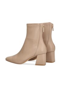 Botas de tobillo beige hechas de cuero suave, con puntera afilada y tacón cuadrado grueso. Cierre de cremallera en la parte posterior con herrajes en tono dorado.