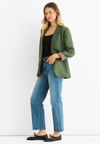 Blazer verde oliva con stampa leopardata sulle maniche, abbinato a jeans a gamba dritta blu e ballerine nere, con un semplice top nero.