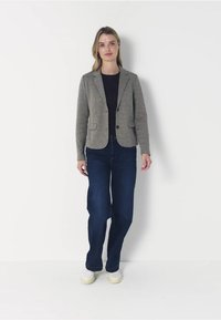 Šedý strukturovaný blejzr se dvěma knoflíky, v kombinaci s tmavomodrými širokými kalhotami a bílými teniskami. Minimalistický design s klasickým střihem.