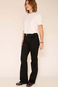 Jean noir évasé en denim, avec des poches avant et une braguette à boutons. Porté avec un t-shirt blanc uni.