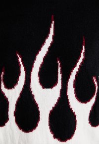 Μαύρο πλεκτό ύφασμα με λευκά σχέδια φλόγας περιγραμμένα σε κόκκινο, που αναδεικνύει μια υφή αντίθεση. Η λεπτομερής κεντητική προ Adds complexity στο σχέδιο.