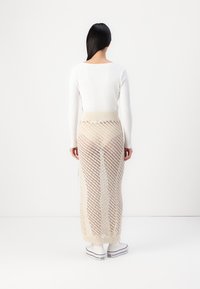 Knelang, semitransparent strikket skjørt i beige med diagonale mønstre. Kombinert med en tettsittende hvit langermet topp og hvite sneakers.