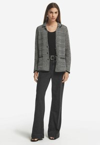 Svart och vit texturerad kavaj med krage, med två framfickor och knappar, parat med svarta utsvängda byxor och sandaler.