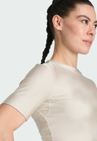 Top de manga corta, ajustado, hecho de una tela ligera y suave en beige, con un cuello redondo y detalles de costura sutiles.