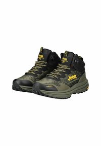 Zapatos de senderismo negros y verde oliva con suelas de goma, parte superior de malla con patrón y acentos amarillos. Incluyen soporte para los tobillos ajustable.