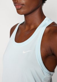 Vaaleansininen urheilutoppi, jossa on pyöreä pääntie, ohuet hihnat ja pieni valkoinen Nike-logo vasemmassa rinnassa.