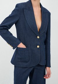 Blazer en denim bleu foncé avec un col cranté, des boutons dorés, deux poches avant et une coupe structurée. Partie d'un ensemble de costume deux pièces.