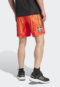 Røde og orange atletiske shorts lavet af letvægtsstof, med sorte sidelister og et logo-patch på venstre side.