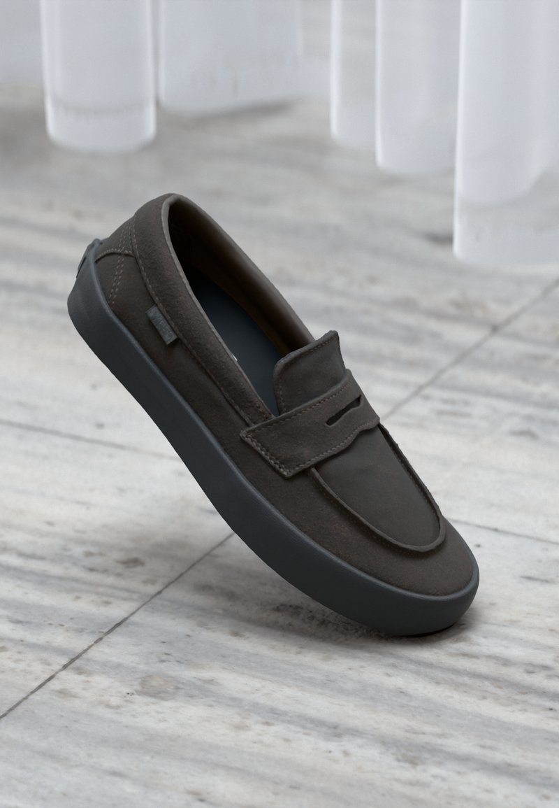 Barna bőr slip-on cipő lekerekített orral, varrott részletekkel és texturált fekete gumitalppal, világos márvány háttér előtt.