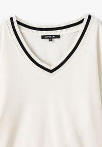 Camiseta de algodón blanca con escote en V y una franja negra acanalada. Textura suave, corte relajado y etiqueta visible en el interior.