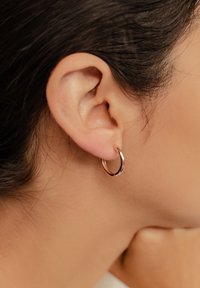 Orecchino a cerchio in oro rosa dal design sottile e circolare. La superficie liscia riflette la luce, pendendo da un orecchio forato. Stile semplice e minimalista.