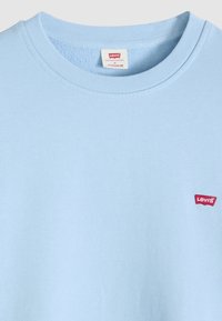 Φωτεινό γαλάζιο βαμβακερό φούτερ με στρογγυλή λαιμόκοψη, που διαθέτει ένα μικρό κόκκινο εμβληματικό ταμπελάκι Levi's  στην αριστερή πλευρά. Απλή και λεία υφή.