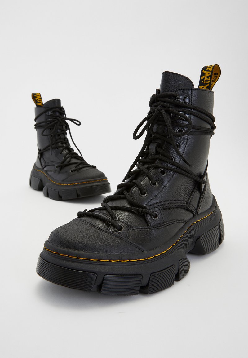 Bottes de combat en cuir noir avec semelles épaisses, dotées de lacets, de coutures jaunes et d'une languette au col. Design élégant et durable.