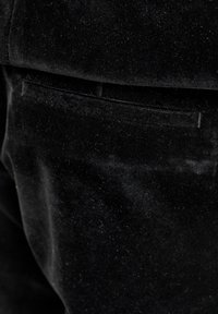 Juodos aksomo medžiaga su švelnia tekstūra, pasižyminti subtiliu blizgesiu. Yra užpakalinė kišenė su siuvimo detalėmis.