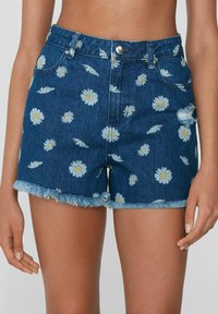 Szorty dżinsowe z postrzępionym wykończeniem, w niebieskim kolorze, pokryte rozrzuconymi białymi wzorami stokrotek. Pięć kieszeni, metalowy guzik.
