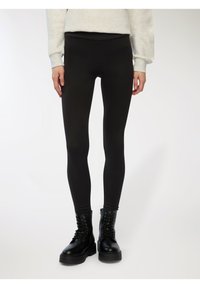 Czarne legginsy z gładkiego, elastycznego materiału, z wysokim stanem. Połączone z czarnymi butami bojowymi, co wprowadza kontrast w fakturze.