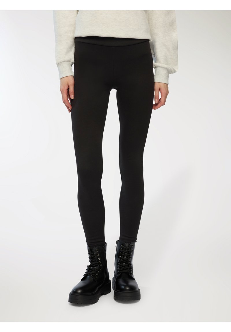 Czarne legginsy z gładkiego, elastycznego materiału, z wysokim stanem. Połączone z czarnymi butami bojowymi, co wprowadza kontrast w fakturze.