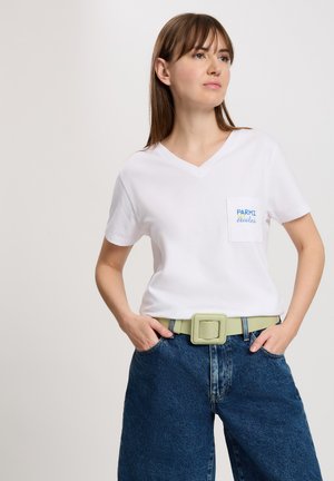 White cotton t-shirt with a v-neck and a pocket featuring blue text. Paired with high-waisted denim shorts and a light green belt.
