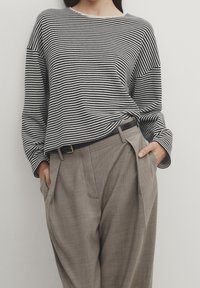 Maglietta a maniche lunghe a righe bianche e nere abbinata a pantaloni beige plissettati. La maglietta presenta una vestibilità ampia e un collo rotondo.