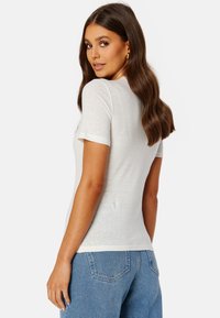 T-shirt bianca a maniche corte con una consistenza morbida e un design aderente, mostrata da dietro. Abbinata a jeans in denim blu a vita alta.