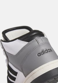 Sneaker alta bianca e grigia con tomaia in pelle liscia, caviglia imbottita, accenti neri e suola in gomma testurizzata con dettagli del logo.