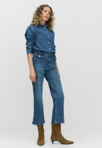 Koszula dżinsowa w średnim niebieskim kolorze z kołnierzykiem, zapinana na guziki, z długim rękawem. Połączona z dżinsami wysokim stanie w niebieskim kolorze oraz jasnobrązowymi botkami za kostkę.
